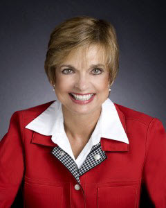 Colleen Burcar - Head-and-shoulders portrait of a smiling woman with short blond hair, wearing a red blazer over a white collared shirt.