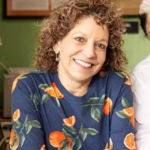 Lisa Brancato - Smiling woman with curly hair in a navy floral shirt, seated at a table in a casual setting.