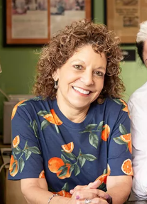 Lisa Brancato - Smiling woman with curly hair in a navy floral shirt, seated at a table in a casual setting.