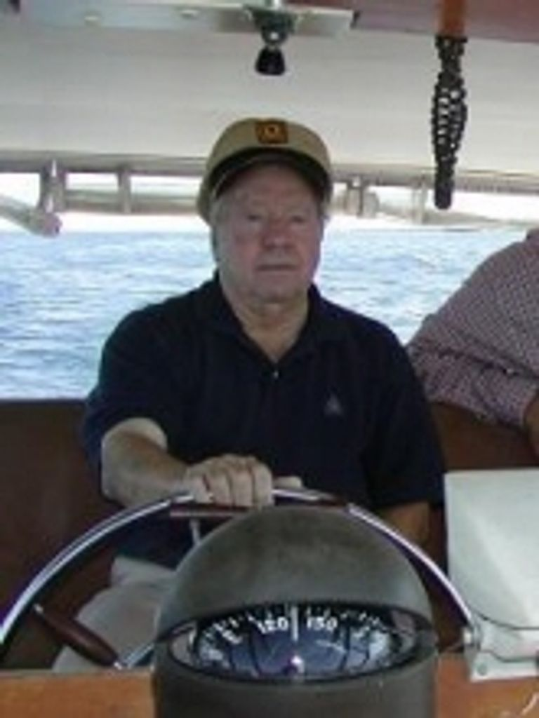 burganwebp - BroadcastingVault.com Jim Burgan - Man in a beige cap steering a boat at sea, with the helm and water in the background.