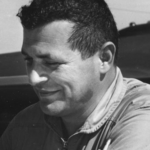 Black-and-white portrait of a man smiling slightly, looking downward to the left.