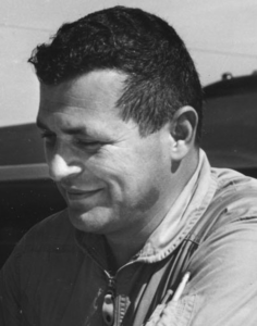 Black-and-white portrait of a man smiling slightly, looking downward to the left.