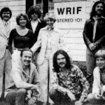 WRIIF - Group of people posing outside a building with a WRIF STEREO 101 sign in the background (black-and-white photo).